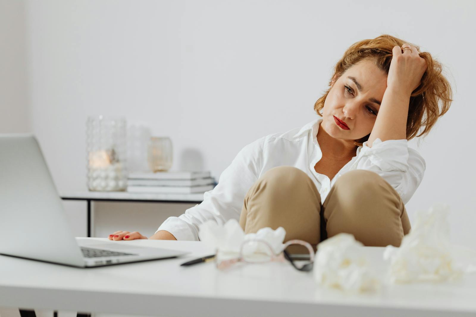 A woman looks stressed while working remotely from home, surrounded by tissues.