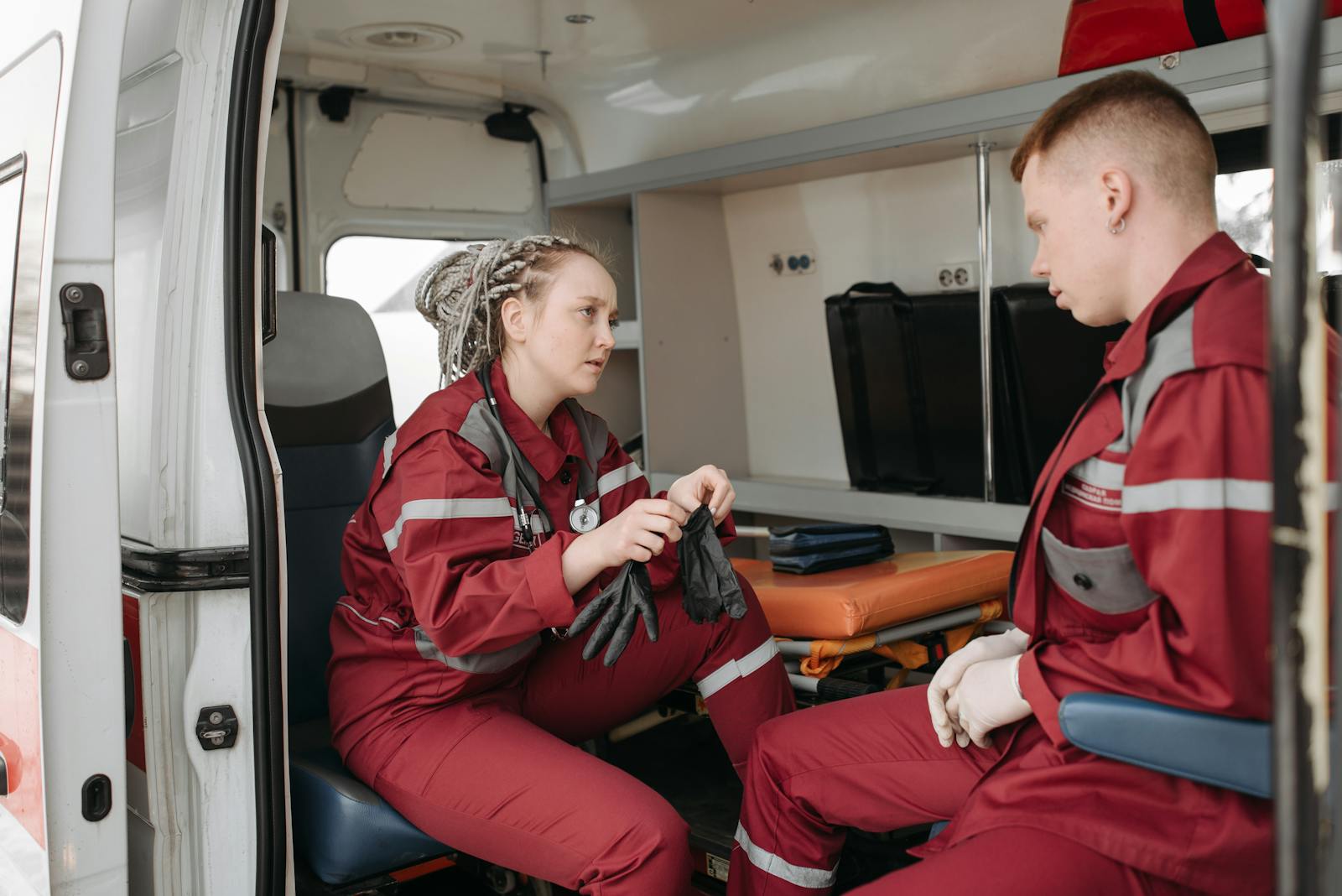 Two paramedics in uniform preparing equipment inside an ambulance.