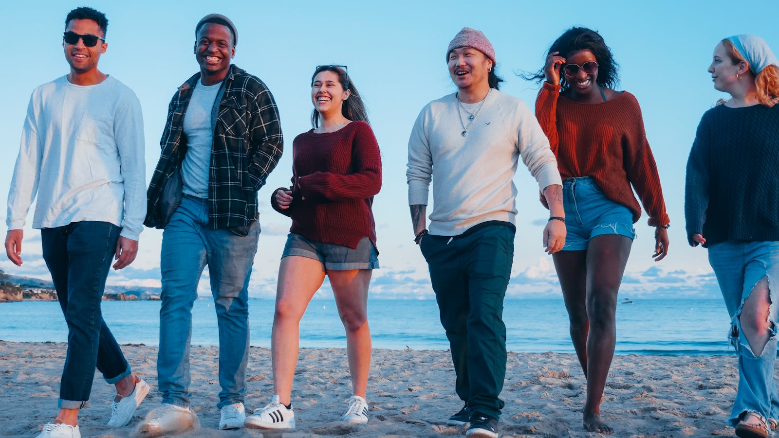 A group of friends enjoys a leisurely walk on the beach at sunset, embodying happiness and togetherness.