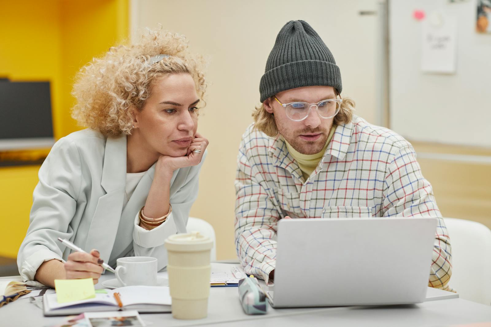 Two professionals discussing ideas at a desk with a laptop and notes in an office setting.