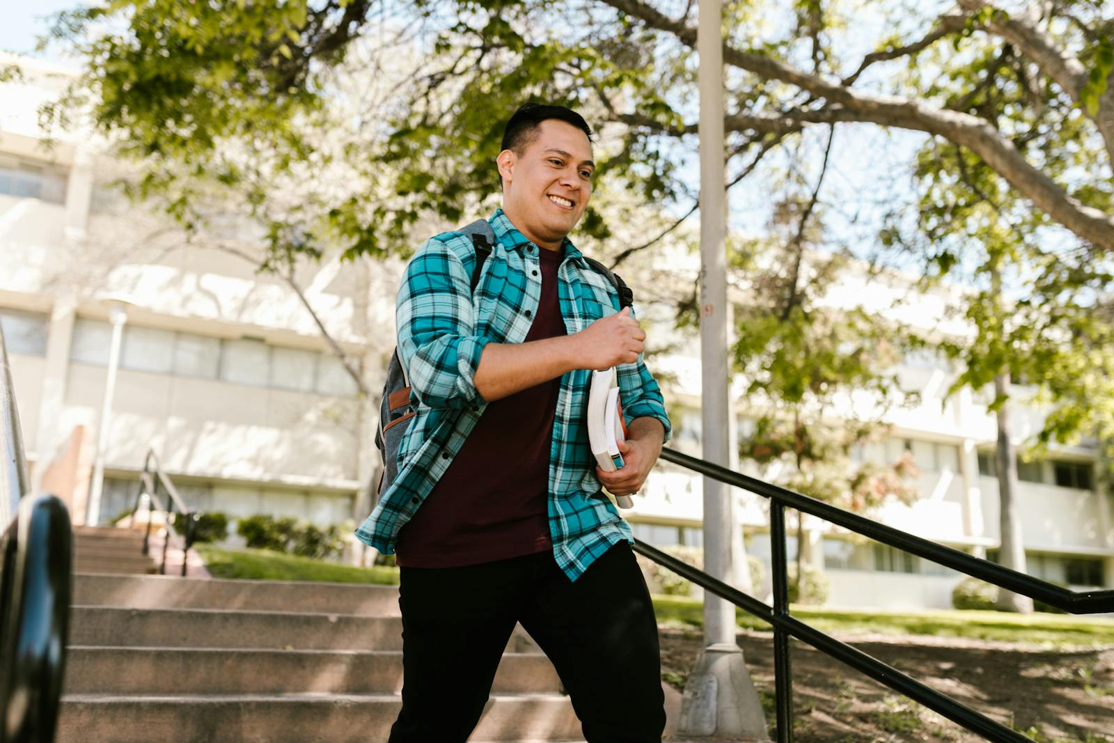 Happy student carrying books outdoors on a sunny day at campus.