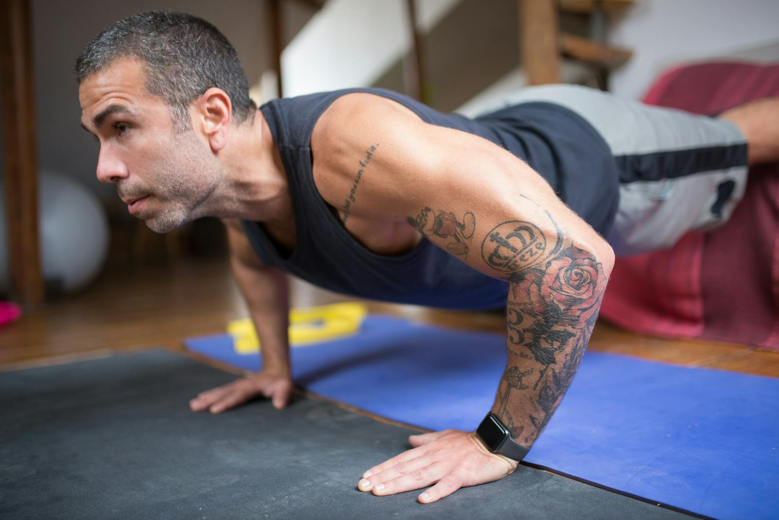 Adult man performing push-ups on a yoga mat, showcasing tattoos and fitness lifestyle.