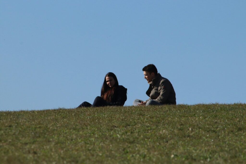 man and woman sitting on green grass field during daytime