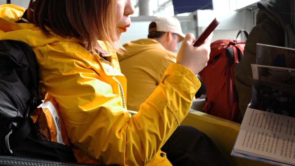 Woman in yellow jacket looks at her phone.