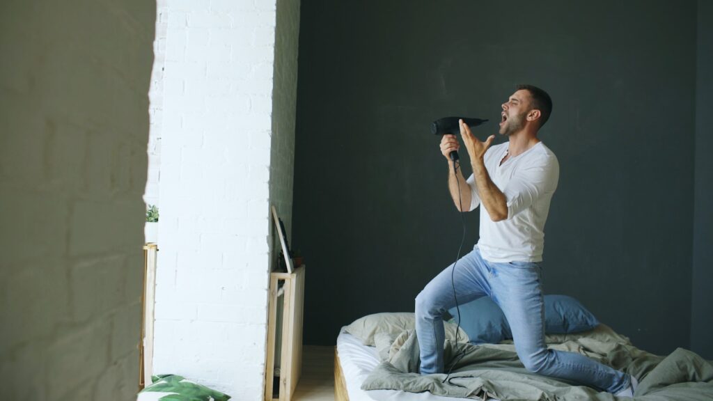Man singing into a remote control on a bed