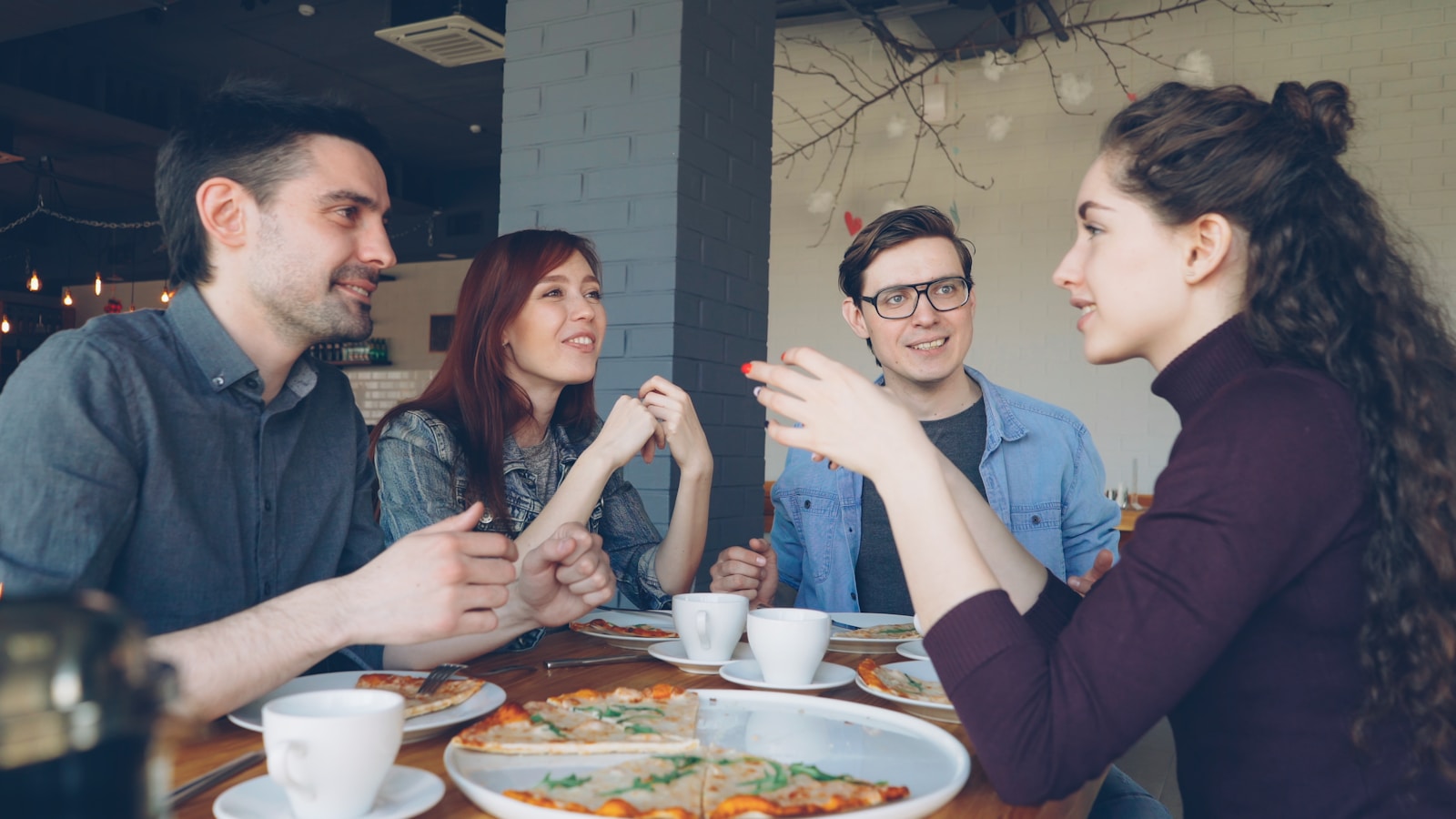 Friends are chatting while sharing pizza at a table.