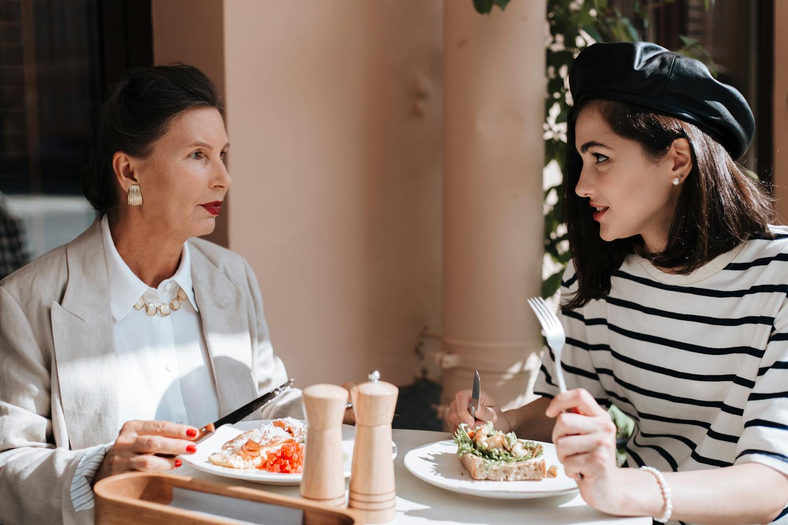 Elegant women enjoying a meal at an outdoor cafe. Fashionable style and serene atmosphere.