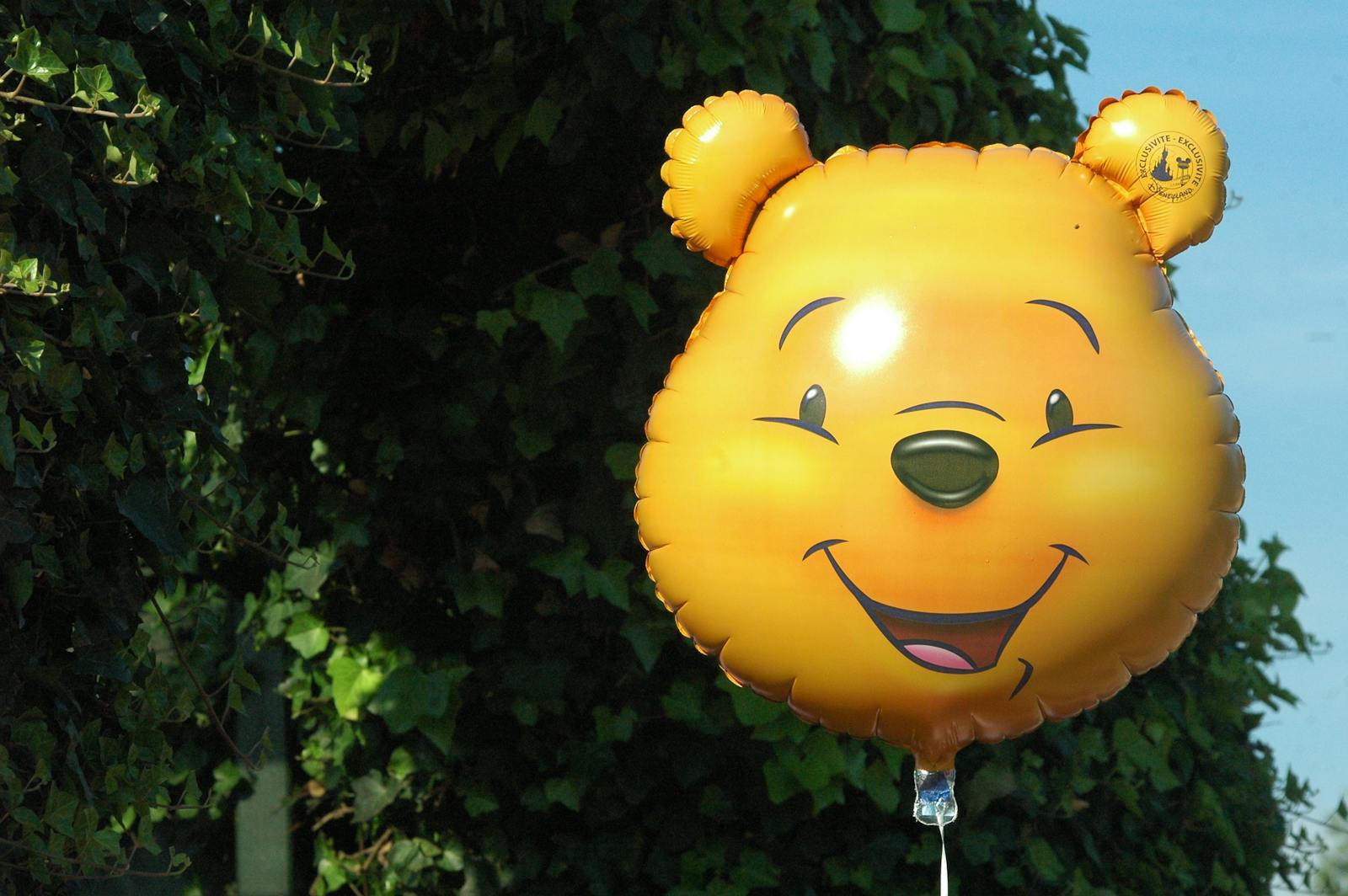A vibrant yellow balloon shaped like a cartoon character set against leafy green foliage outdoors.
