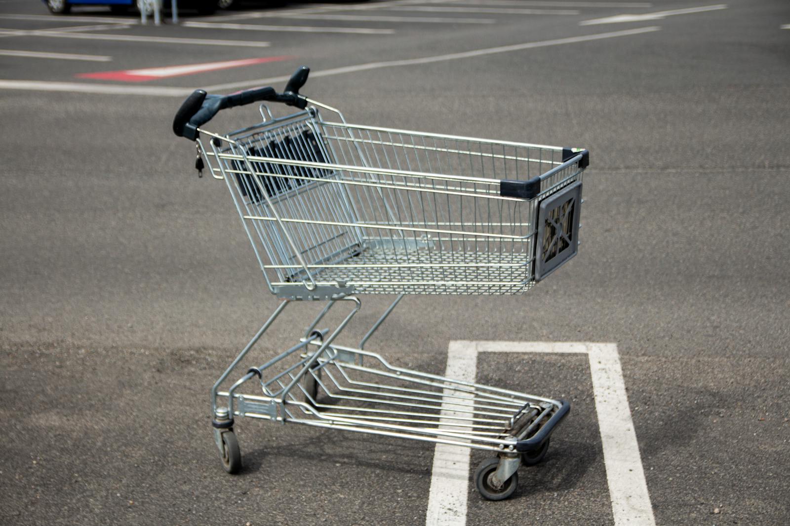 A lone shopping cart sits idle in an empty parking lot on a sunny day.