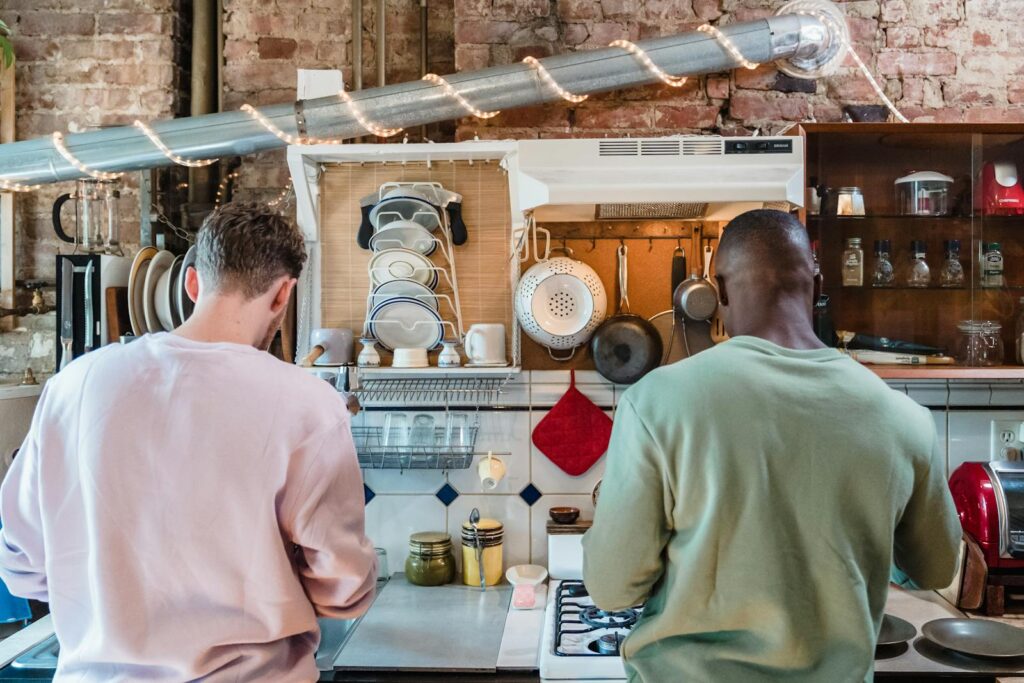 Two men cooking in a rustic kitchen, showcasing a cozy domestic scene with warm lighting.