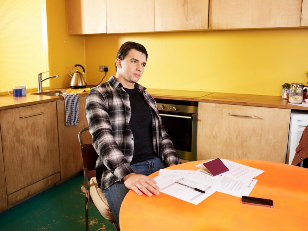 Man sitting at a kitchen table with documents and a passport, contemplating.