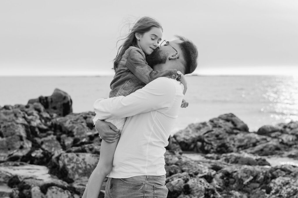 Father joyfully holds his daughter by the sea.