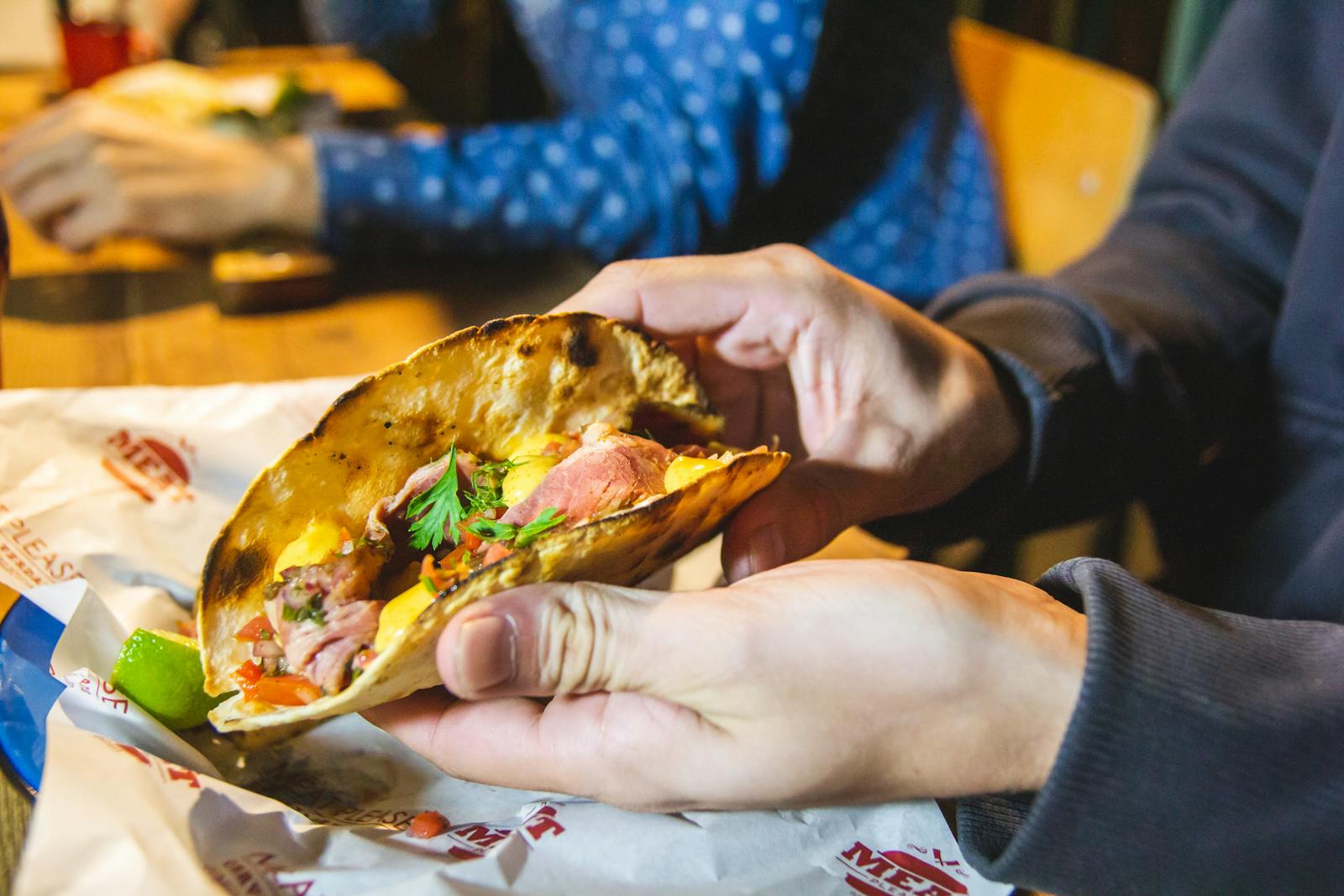 Closeup of a delicious beef taco with fresh ingredients being held at a cozy dinner setting.