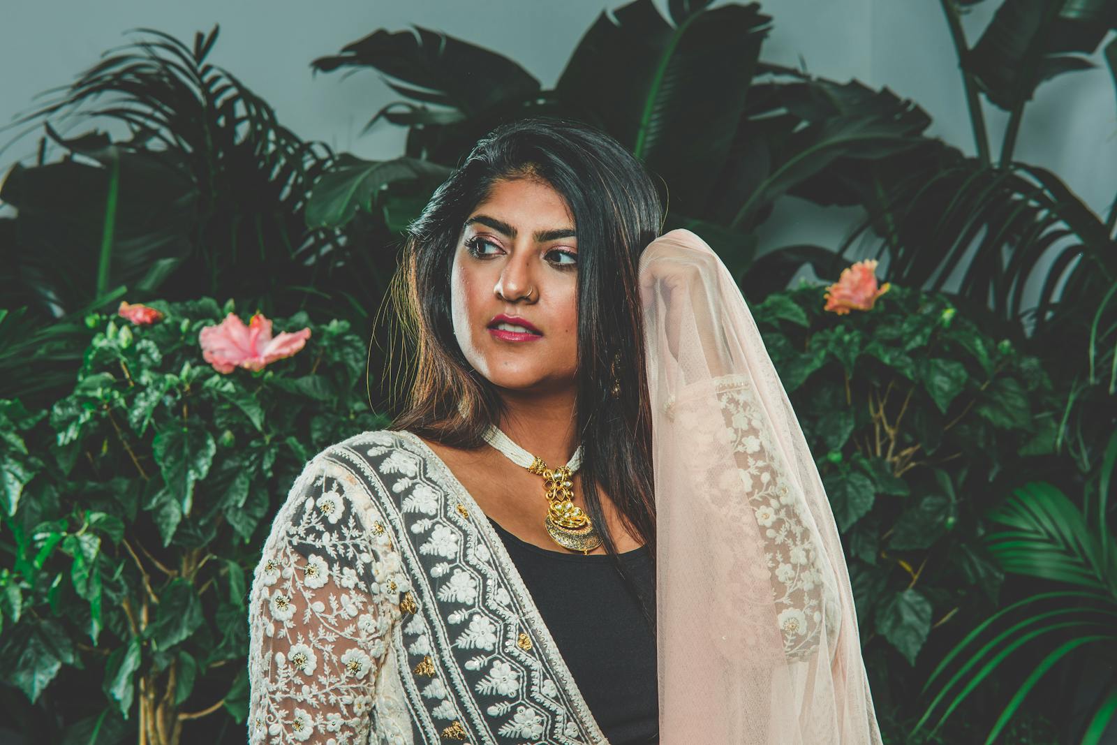 A beautiful South Asian woman poses gracefully in traditional attire with floral background.