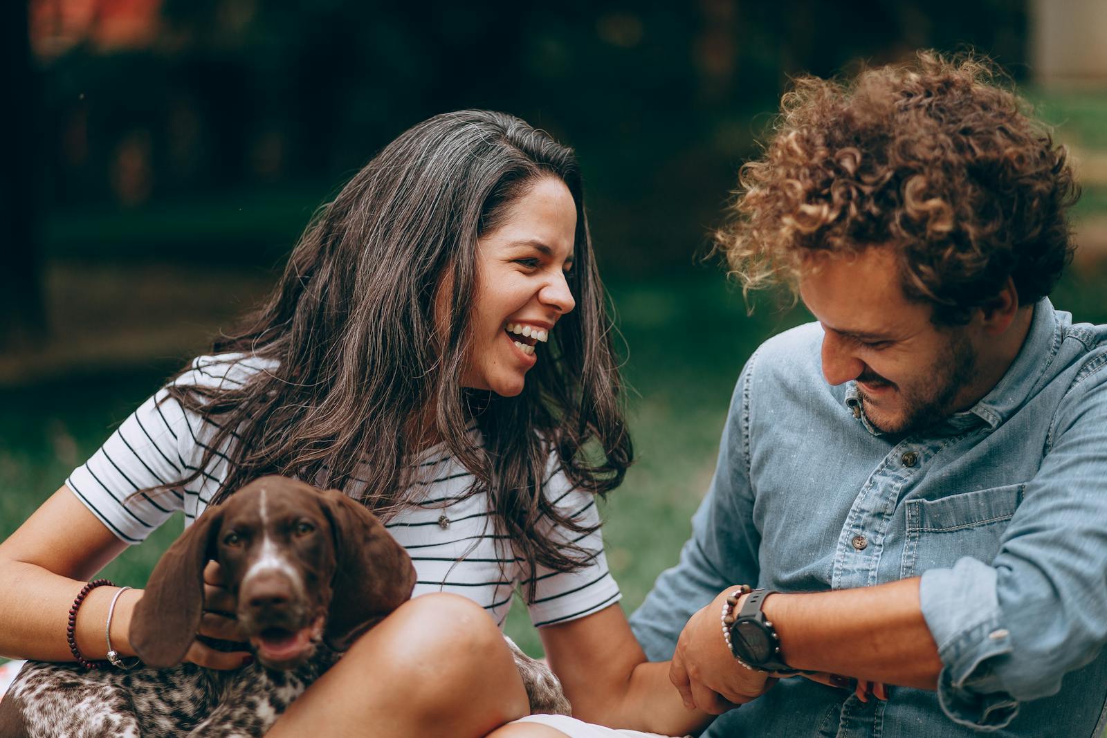 A joyful couple laughing with their dog outdoors, showcasing warmth and companionship.
