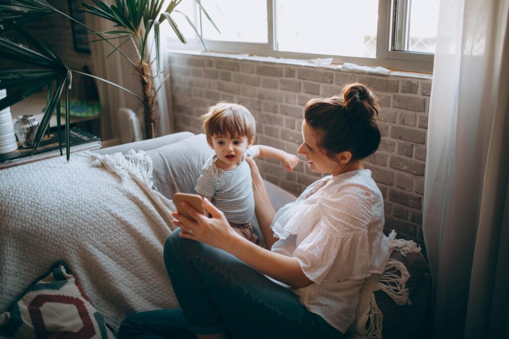 A mother and child bonding on the sofa, enjoying time together with a smartphone in a cozy home setting.