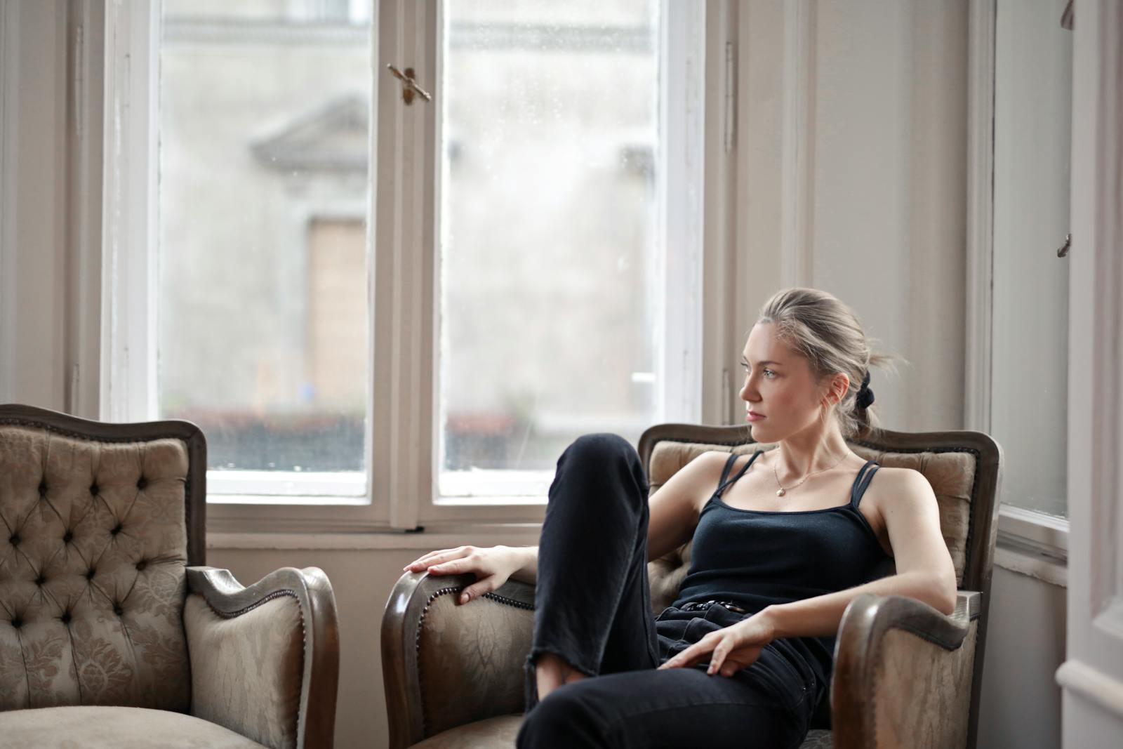 Woman in stylish black top lounging in a chair by the window, Budapest.