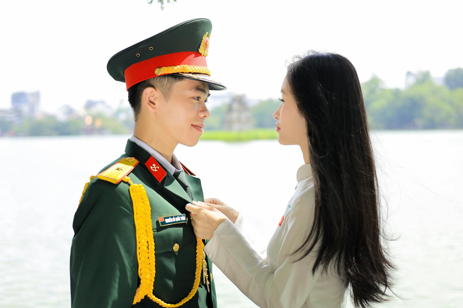 A young couple shares a moment by Hoan Kiem Lake, Hanoi, in military attire.