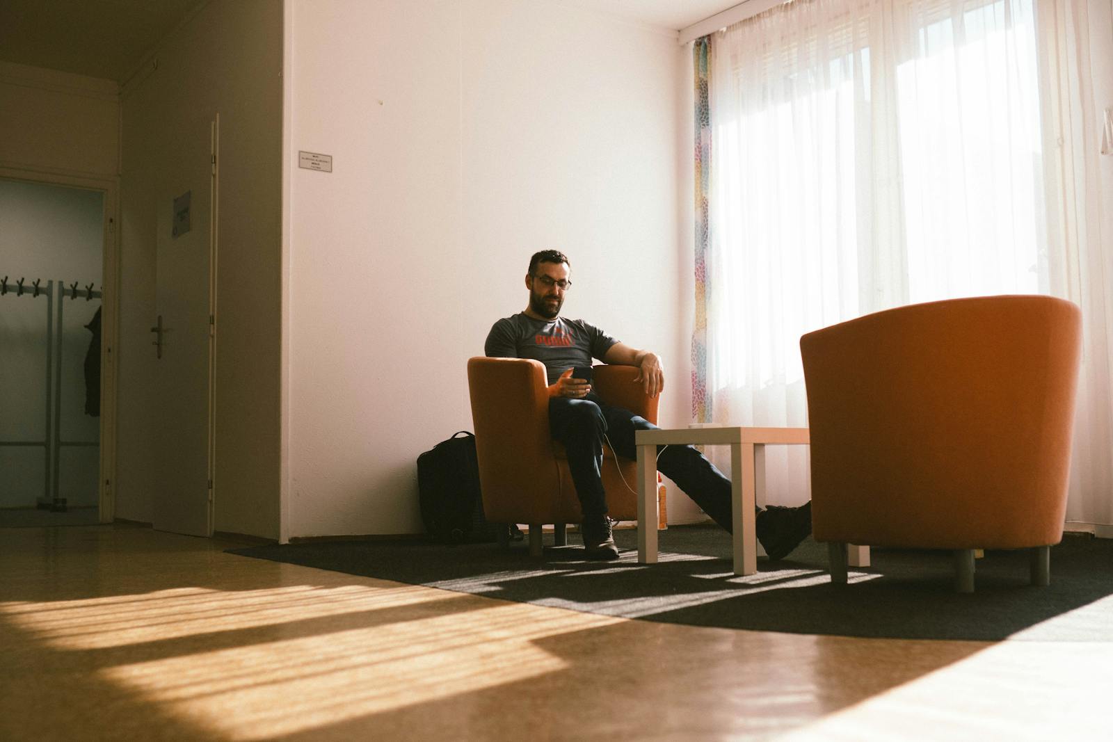 A man sits in a modern lounge, enjoying sunlight through large windows.