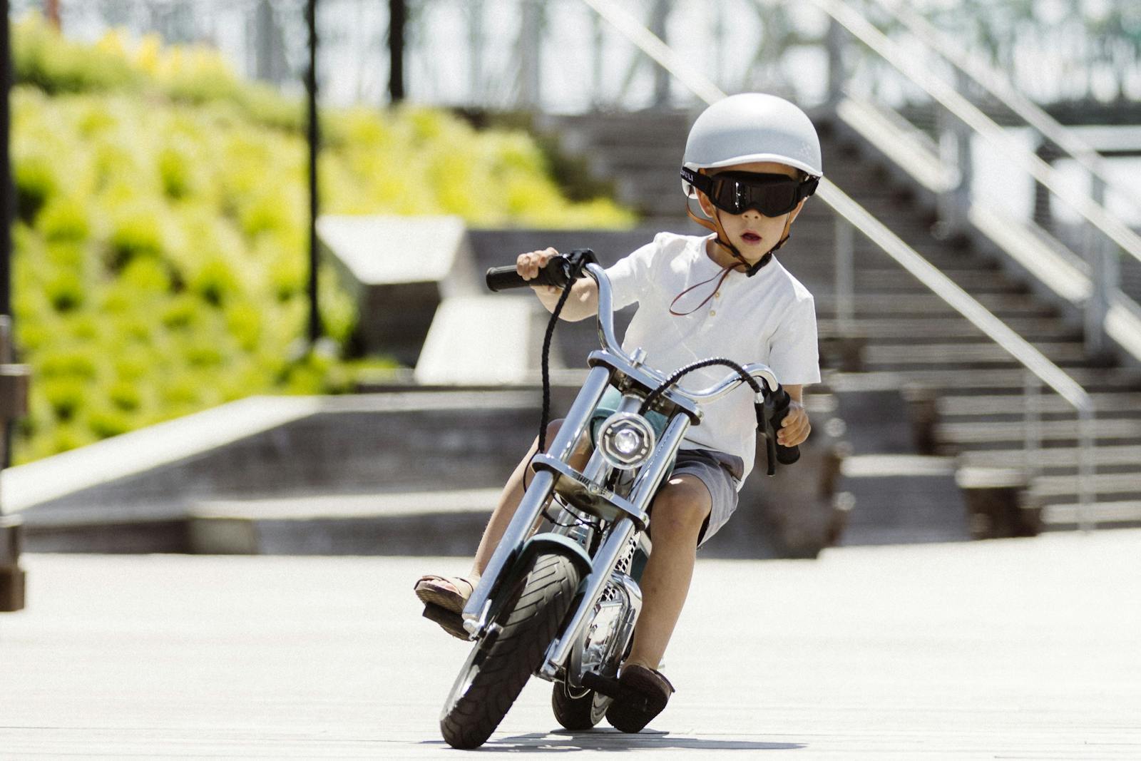 A young child in a helmet rides a miniature motorbike outdoors on a sunny day.