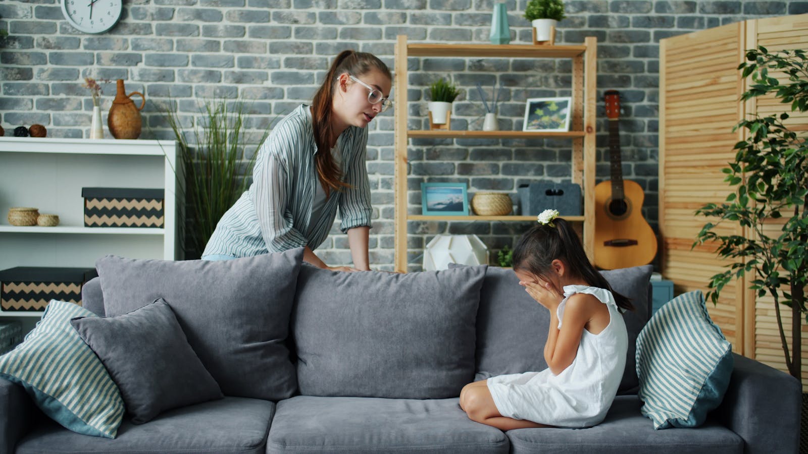 A mother comforts her crying daughter in a cozy living room setting.
