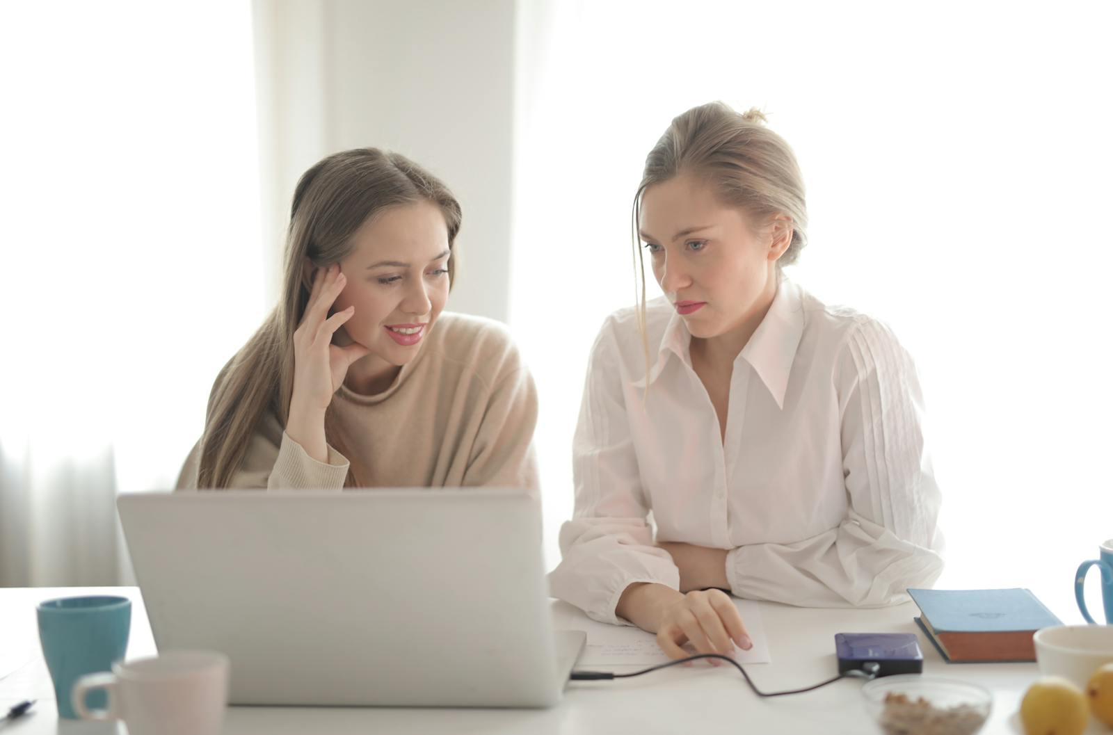 Female workers in casual outfit sitting together at table in bright workplace and thinking of business strategy