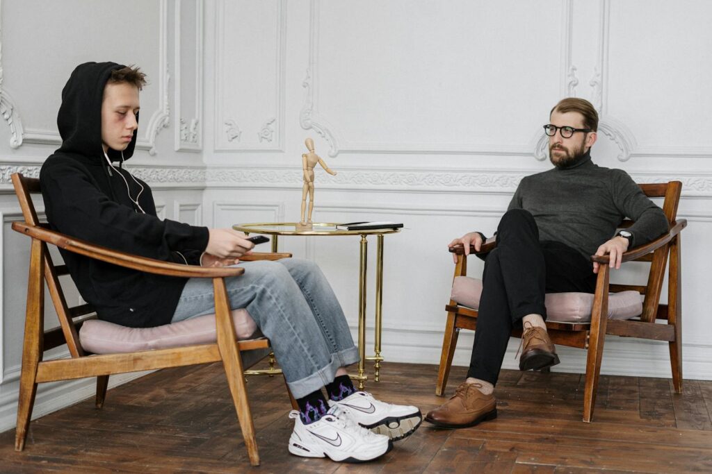 A concerned teenage boy in a hoodie sits with a therapist during a session.