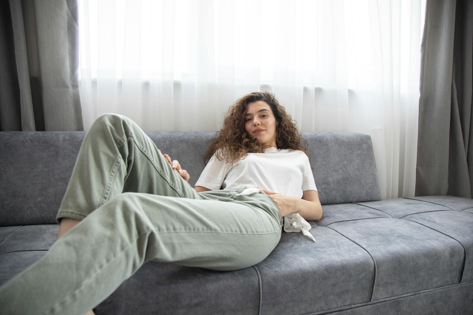 A woman in casual attire relaxing on a sofa in a bright indoor setting.