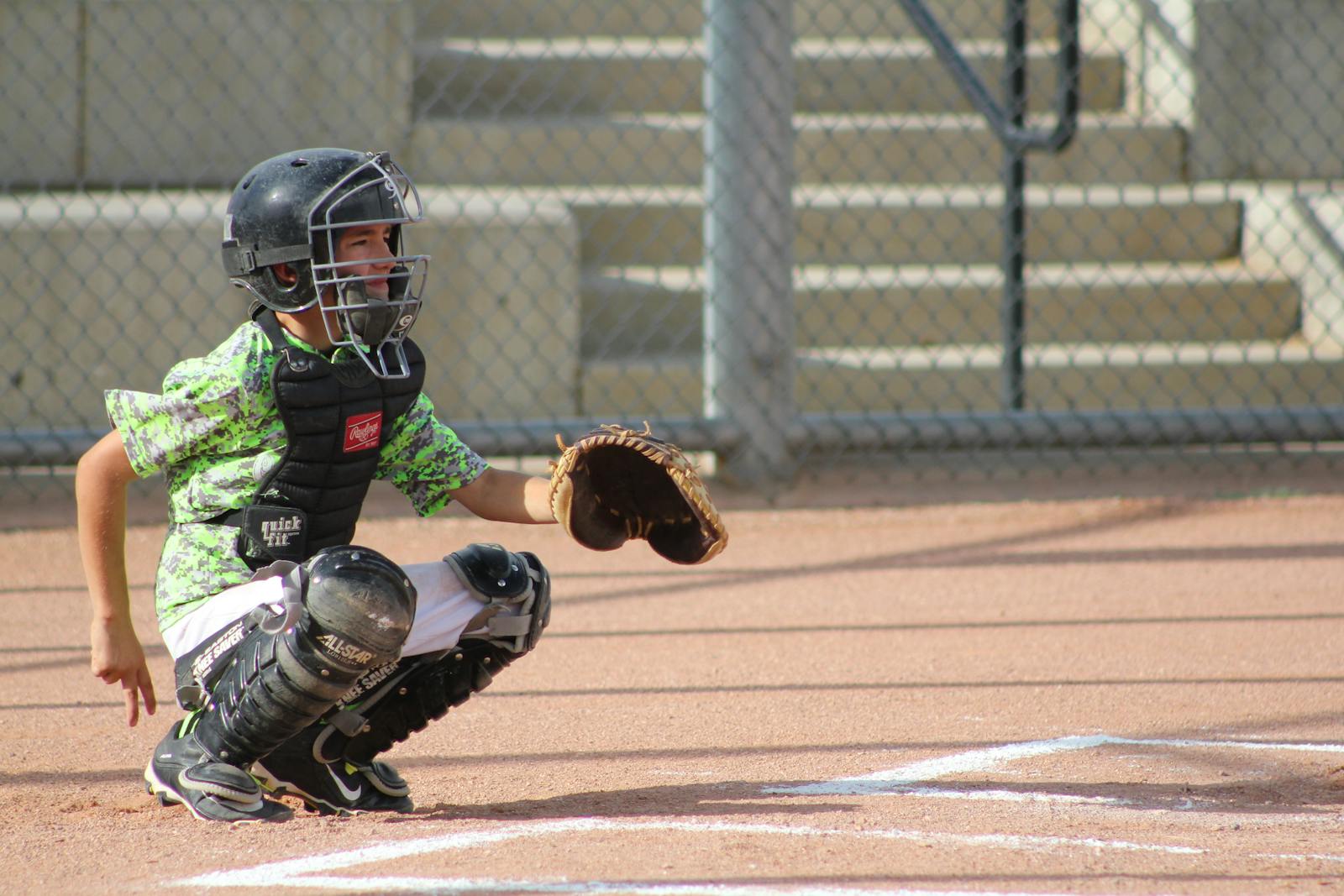 Young boy playing as a baseball catcher, crouched and ready during a daytime game.