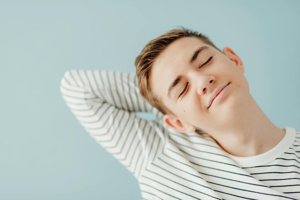 A smiling teenage boy with closed eyes and striped shirt, posing relaxedly.