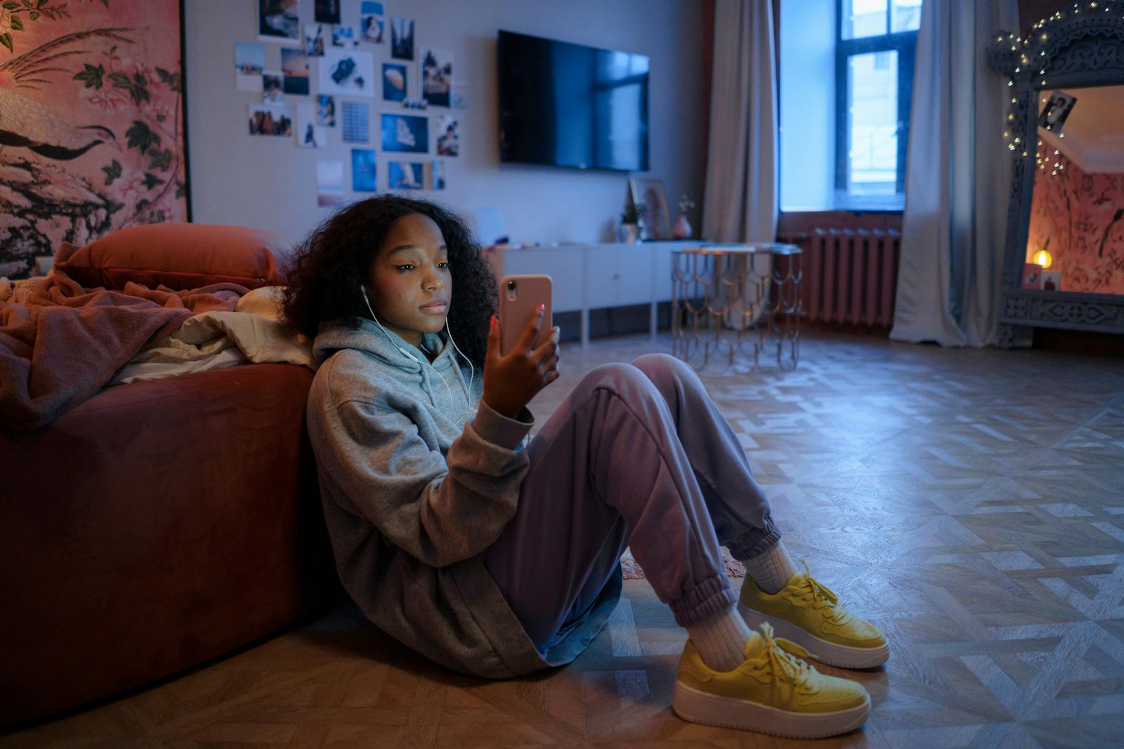 Teenage girl sitting on the floor using a smartphone, relaxed in a cozy room setting.