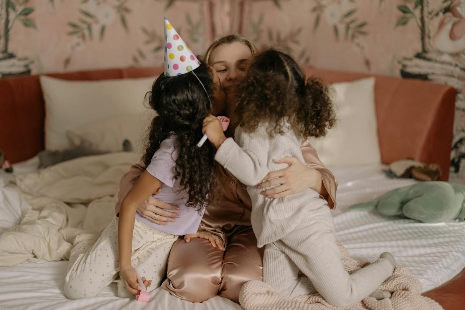 A loving mother shares a tender moment with her two daughters in a cozy bedroom setting, depicting familial warmth.