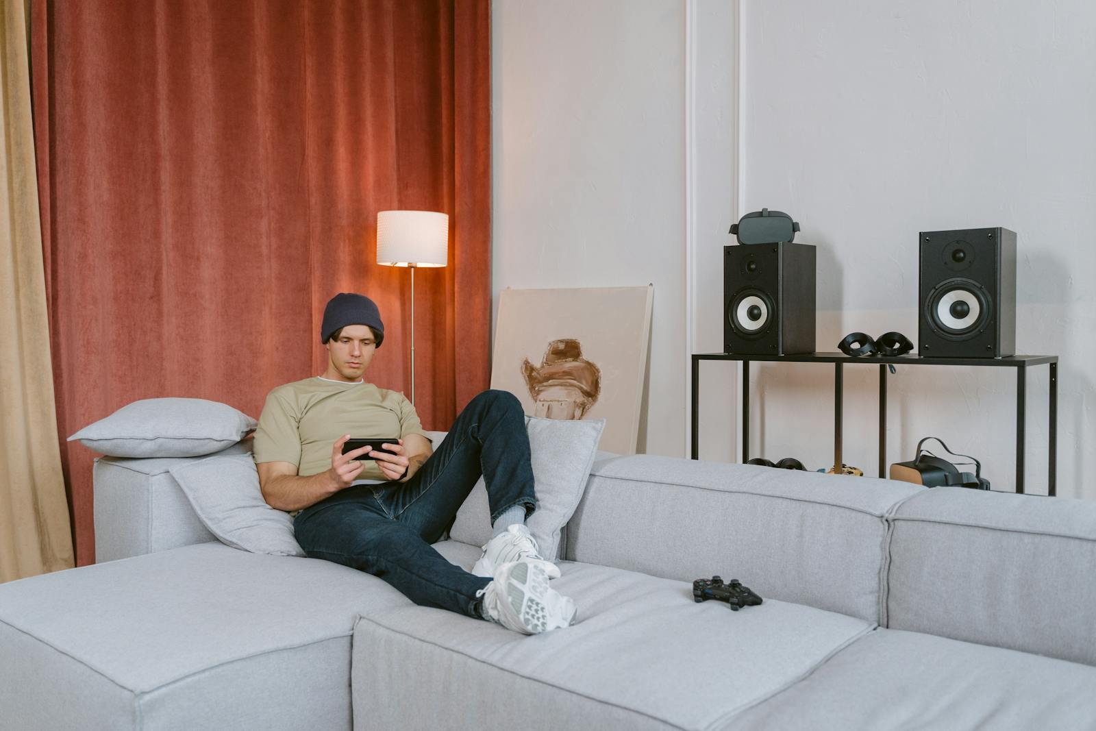 Adult man sitting on a sofa playing with a smartphone in a stylish living room setting.