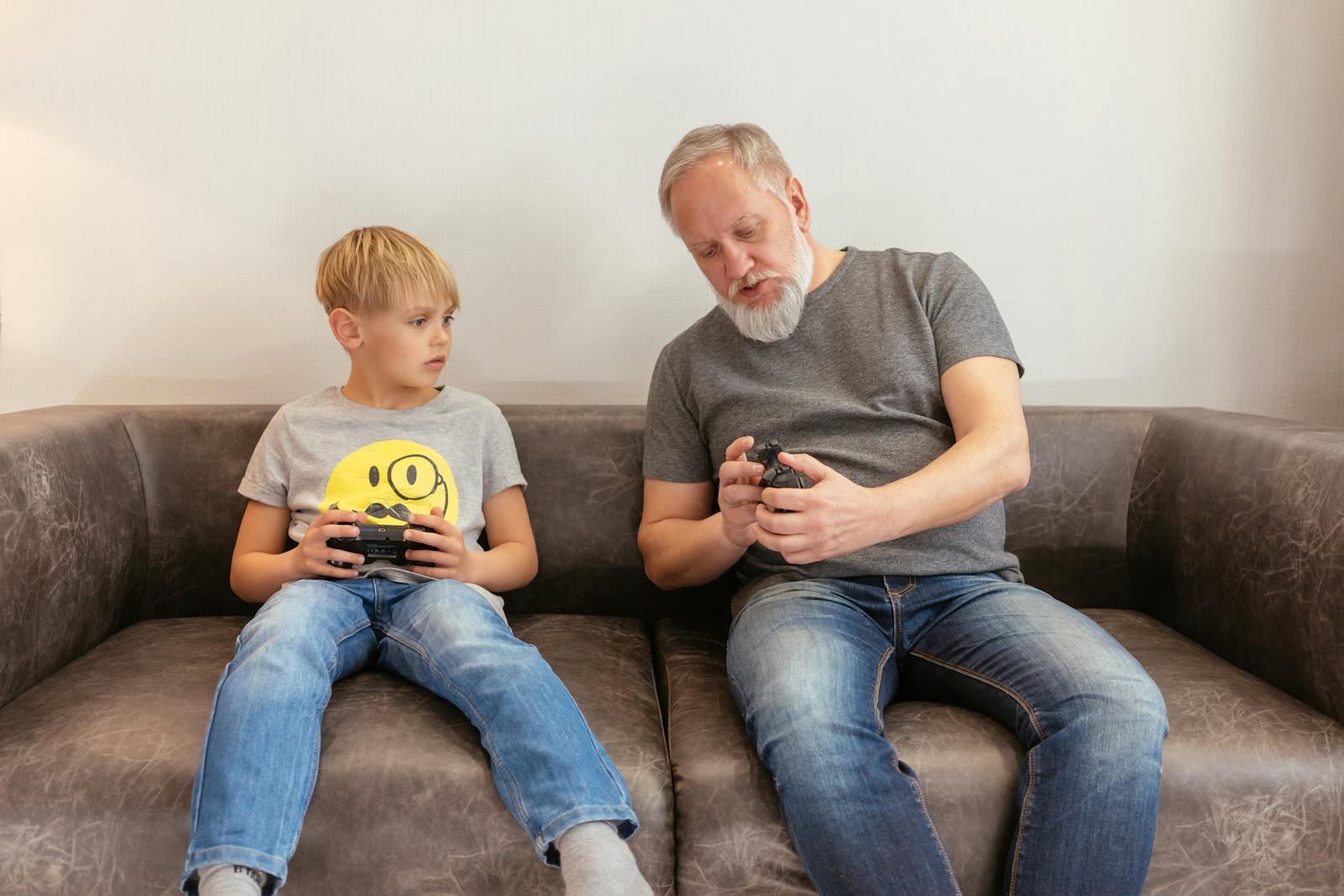 A senior man and child sharing a gaming moment with controllers, indoors on a sofa.