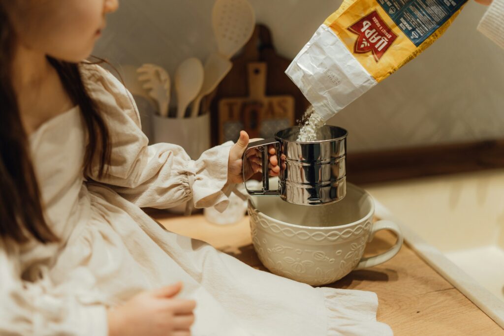A little girl sitting on a kitchen counter pouring milk into a blender