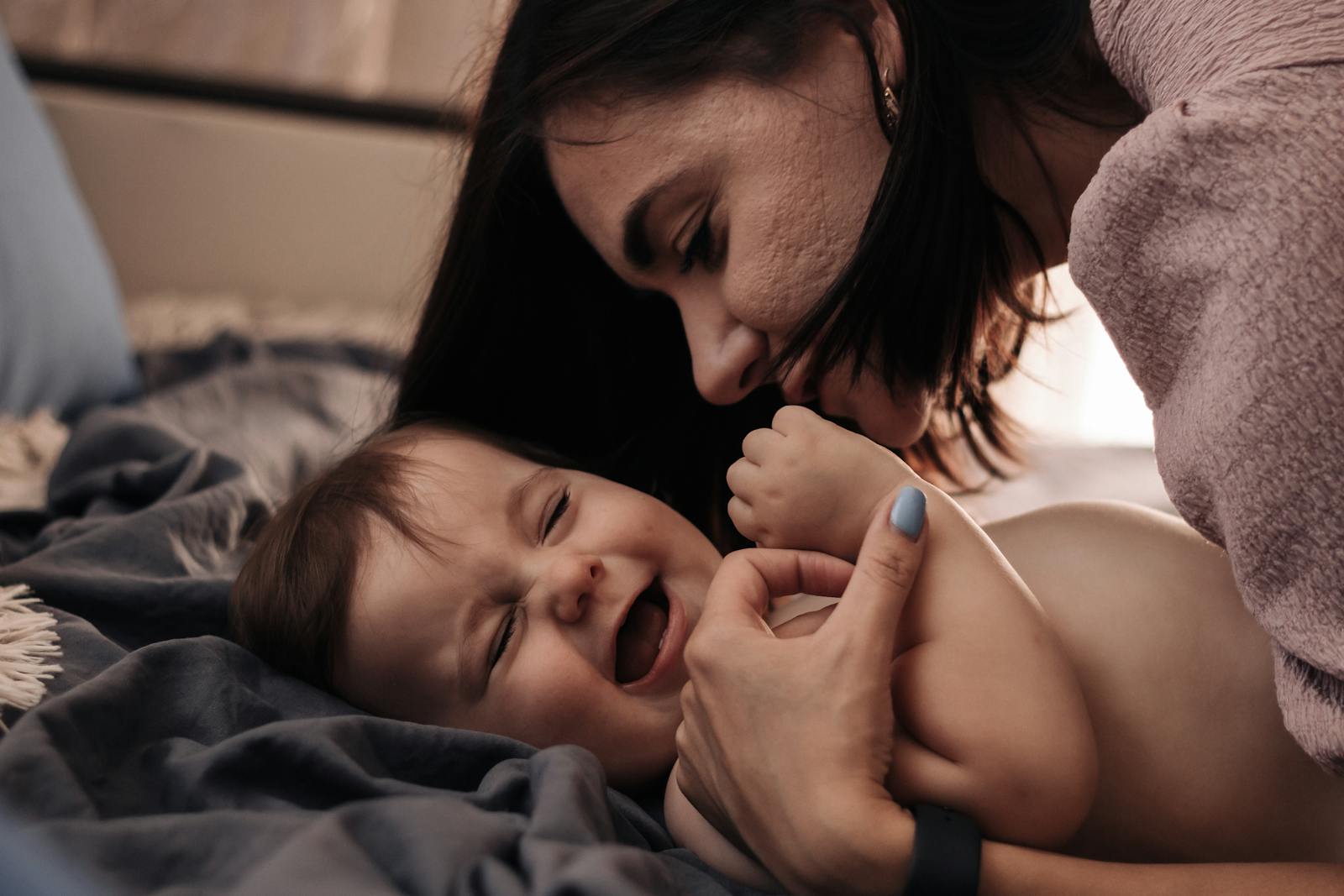 Tender moment between mother and baby, sharing a joyful laugh in a cozy indoor setting.