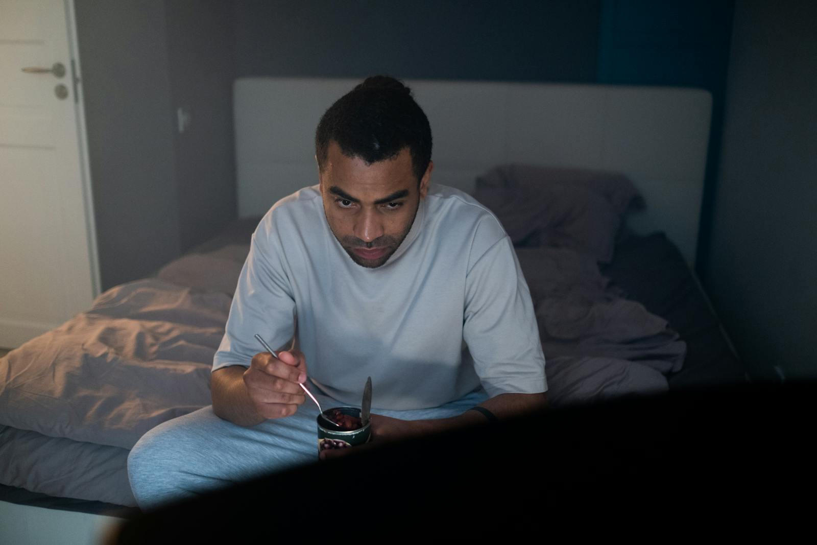 Adult male enjoying a dessert watching TV in a cozy bedroom setting.