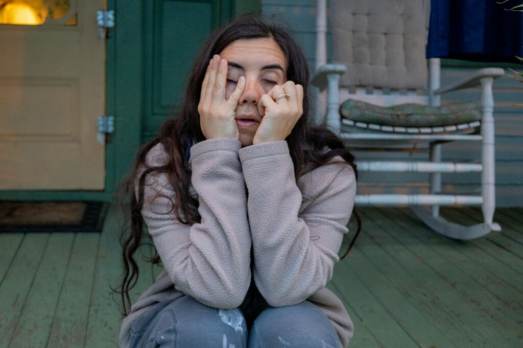 a woman sitting on a porch covering her eyes