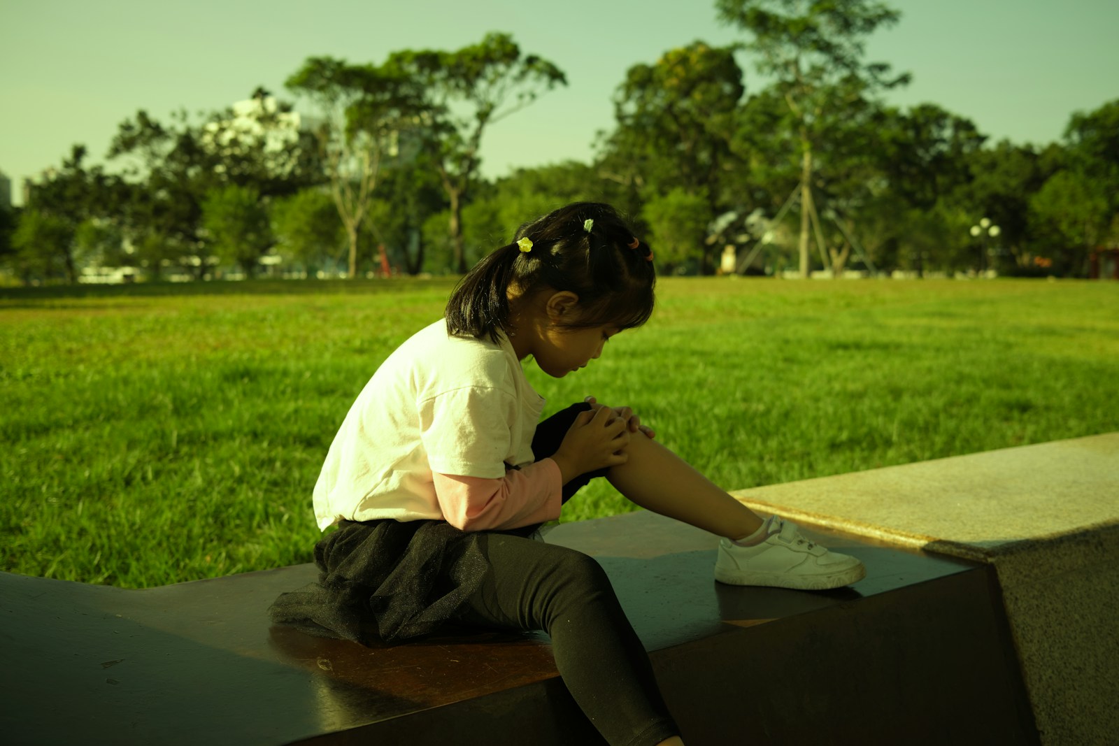a young girl sitting on a bench in a park