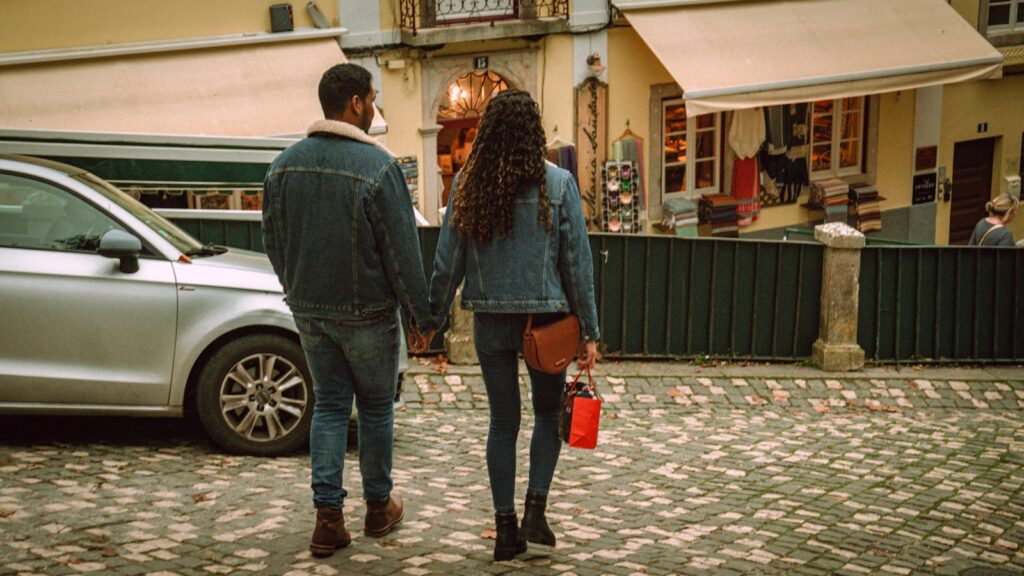 A couple holds hands while walking down street.