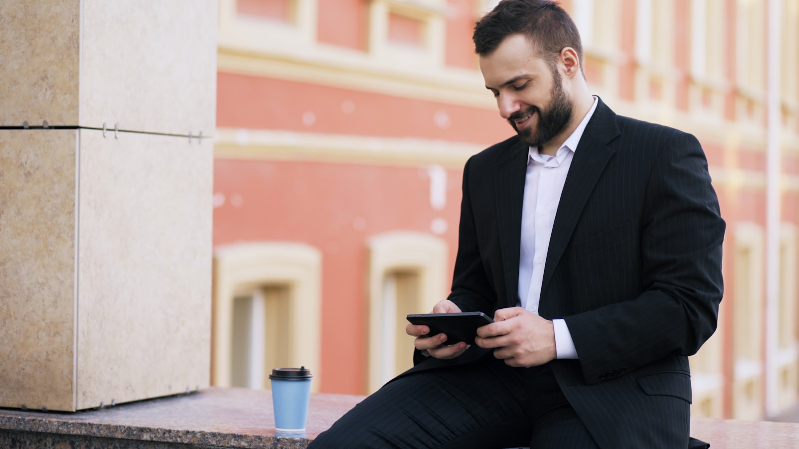 Man in suit using phone with coffee cup nearby.