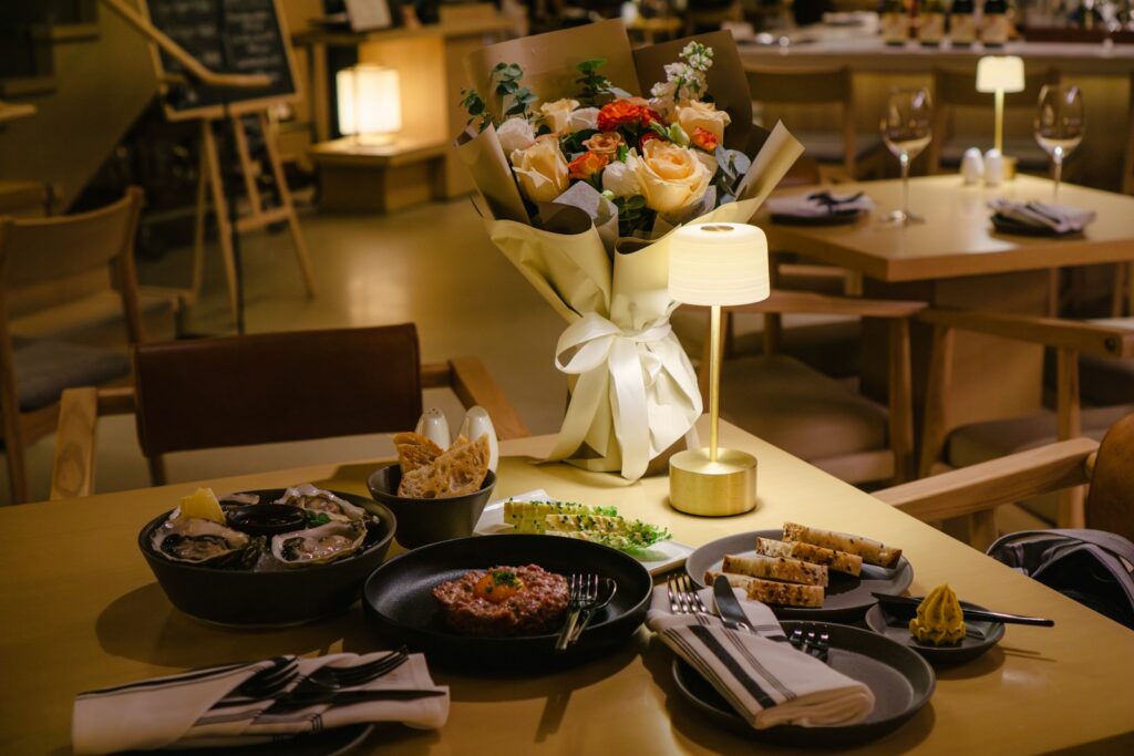 A table setting with food, flowers, and a lamp.