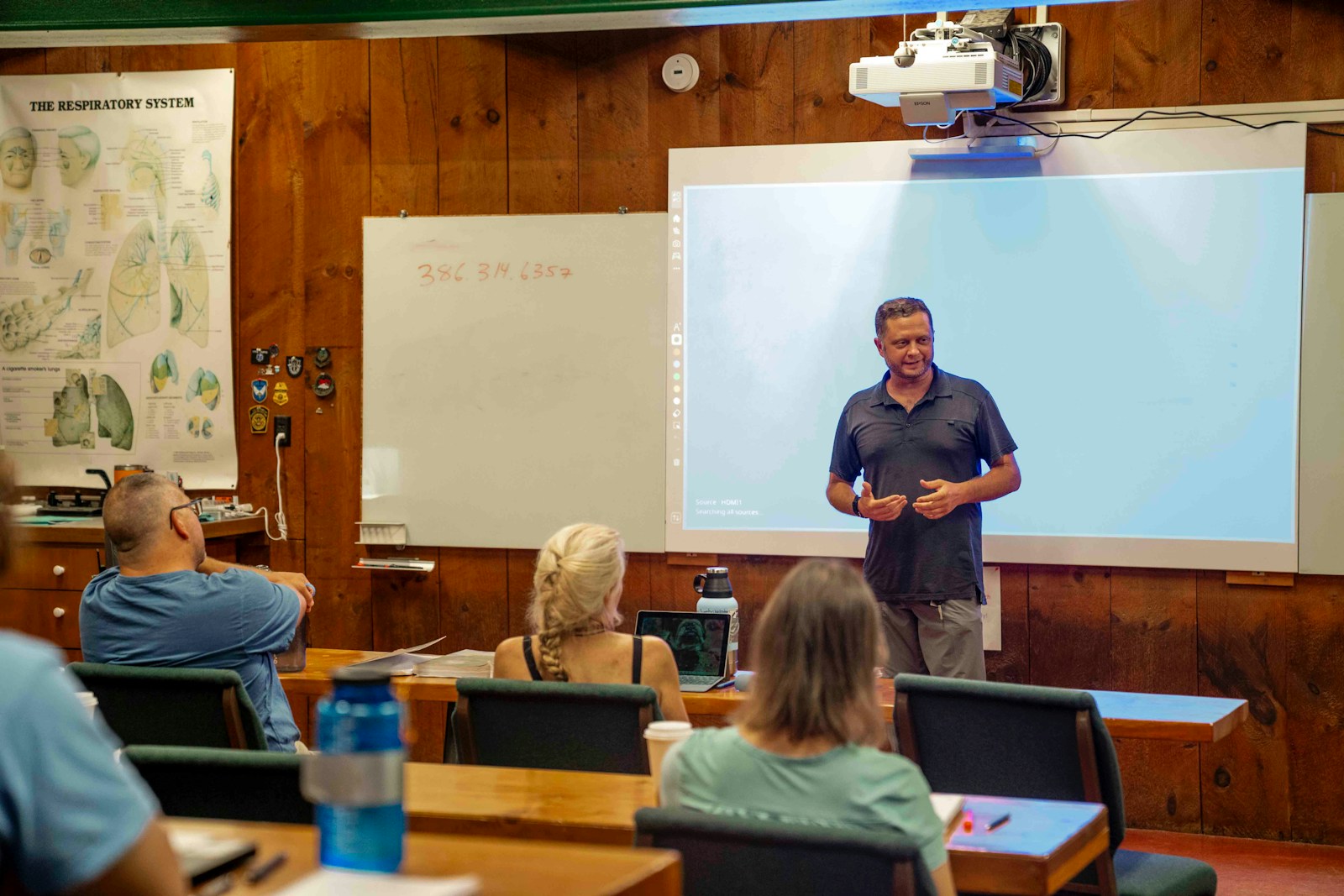 Man presenting to an audience in a classroom setting.