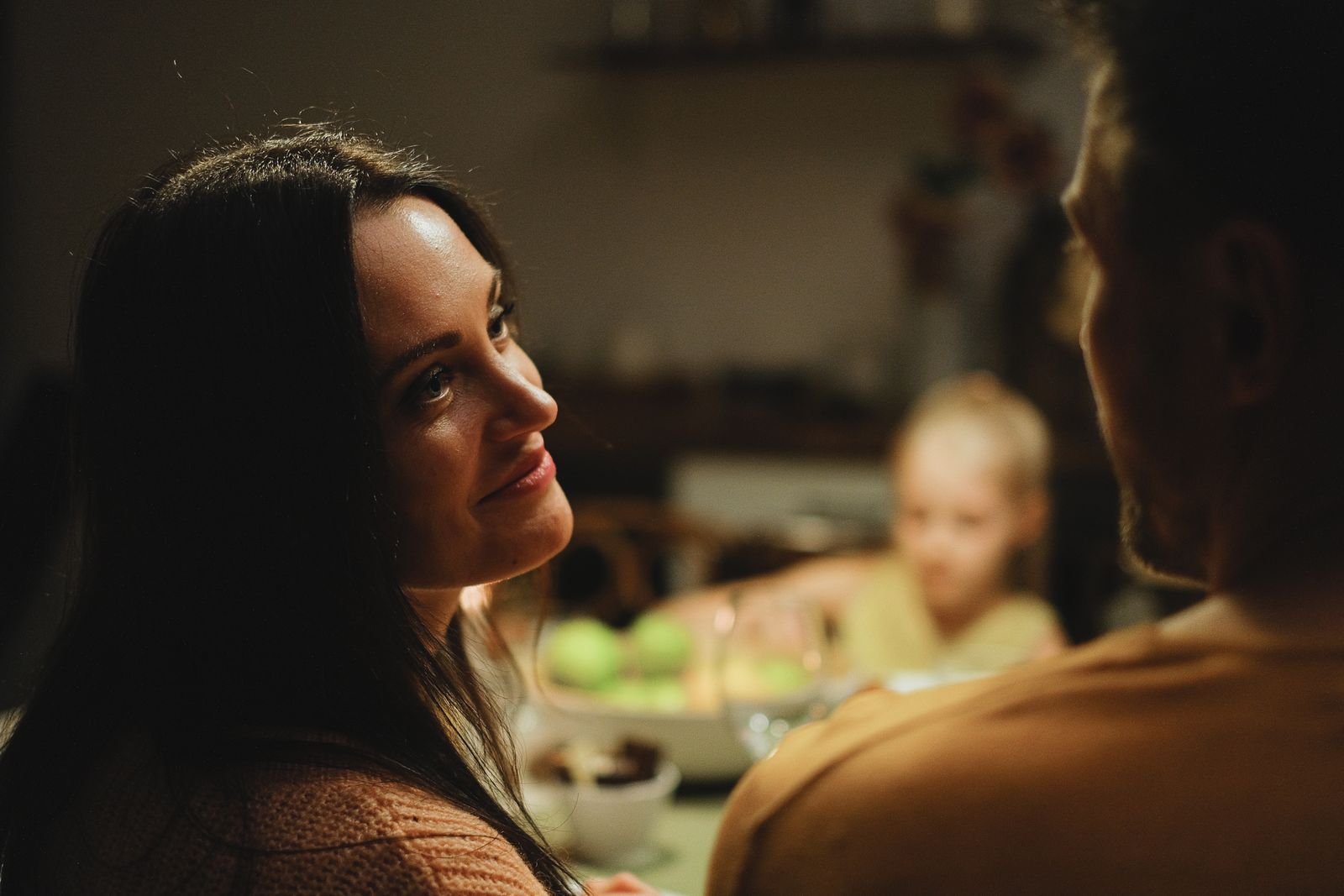 A couple shares a warm moment indoors with a child in the background.