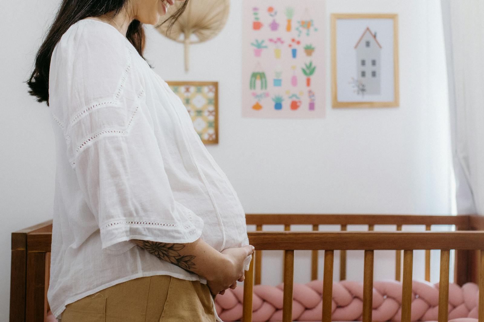 Expectant mother standing beside a wooden crib in a beautifully decorated nursery room.
