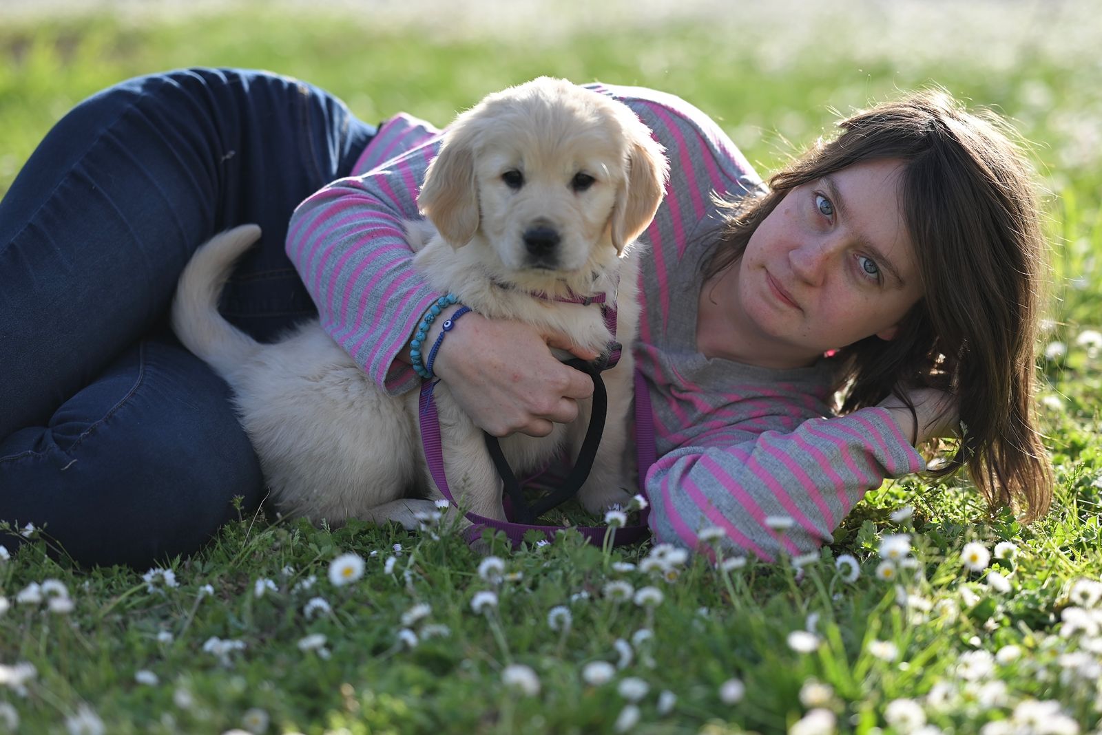 Woman lying on grass cuddling a golden retriever puppy. Captured during daytime in a natural setting.