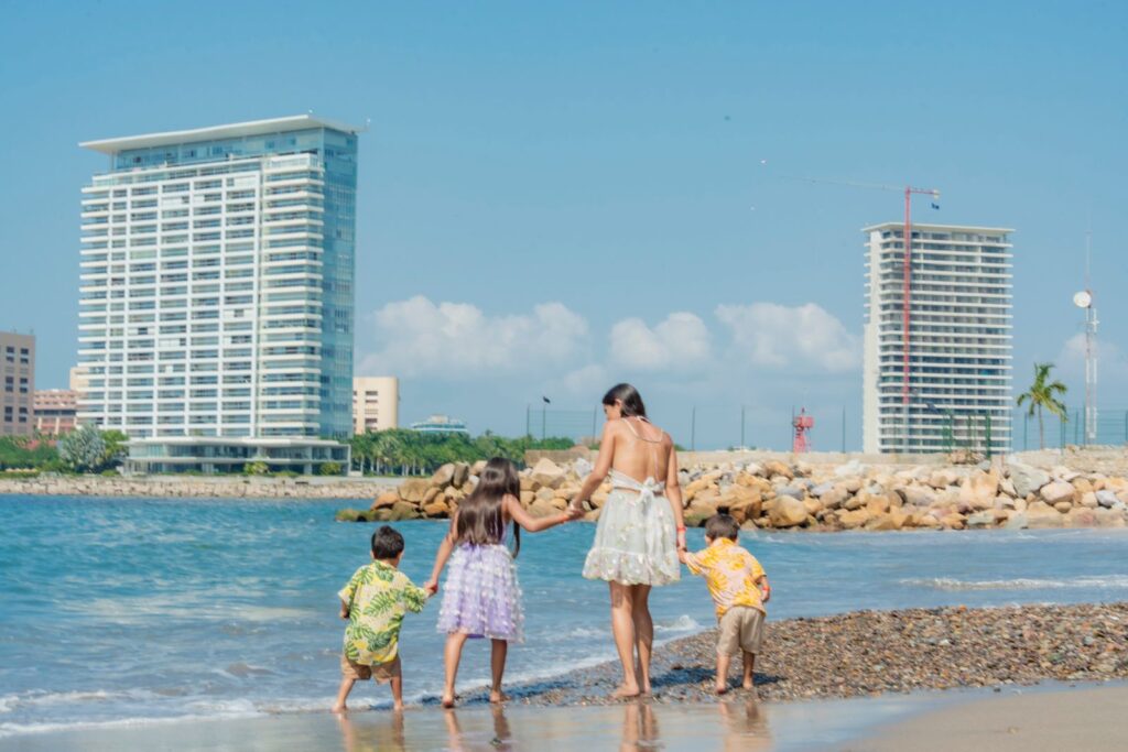 A happy family playing on a sandy beach with modern buildings in the background on a sunny summer day.
