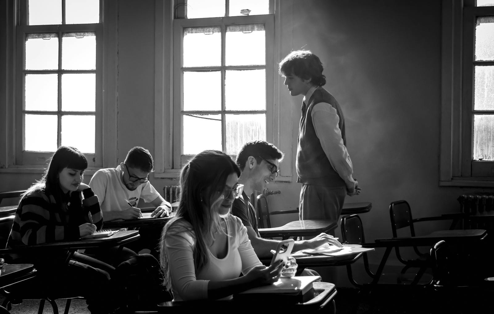 Black and white image of students studying in a classroom with a teacher present.