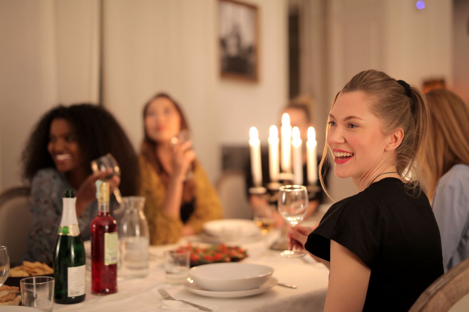 Group of diverse women enjoying a candle-lit dinner, smiling and chatting.