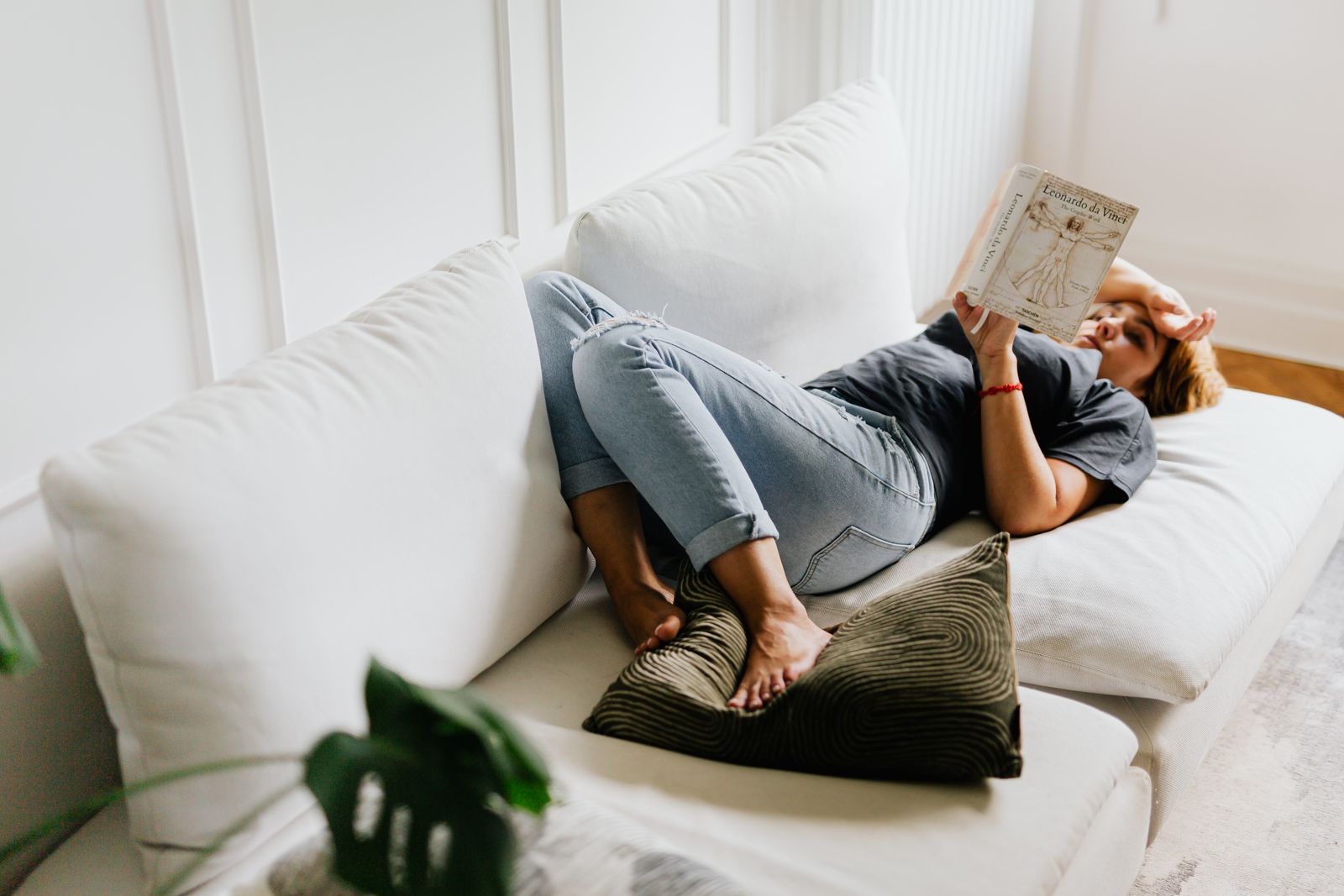 A woman relaxing on a white sofa, reading a book in a peaceful home setting.